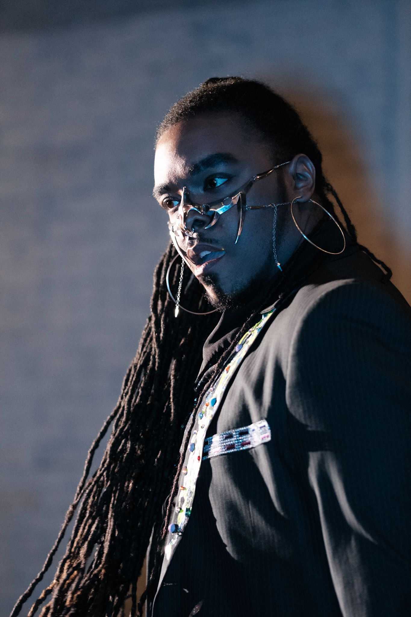 Dramatic portrait of performer with dreadlocks and hoop earrings in blue lighting.