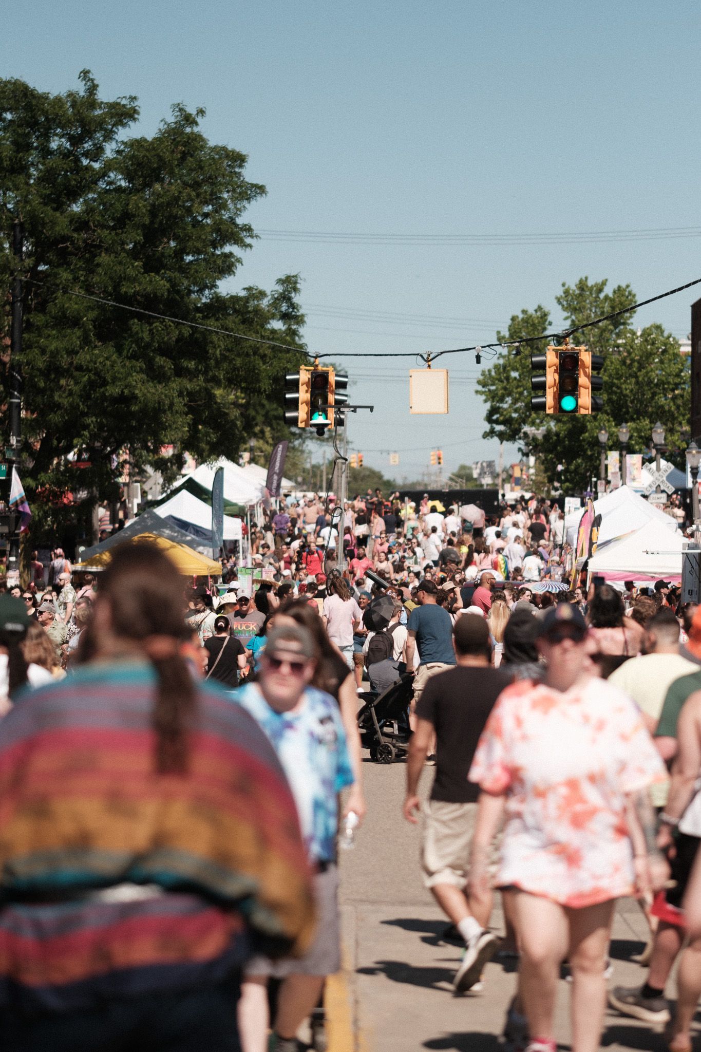 Crowded summer street festival with tents and traffic lights under blue sky.