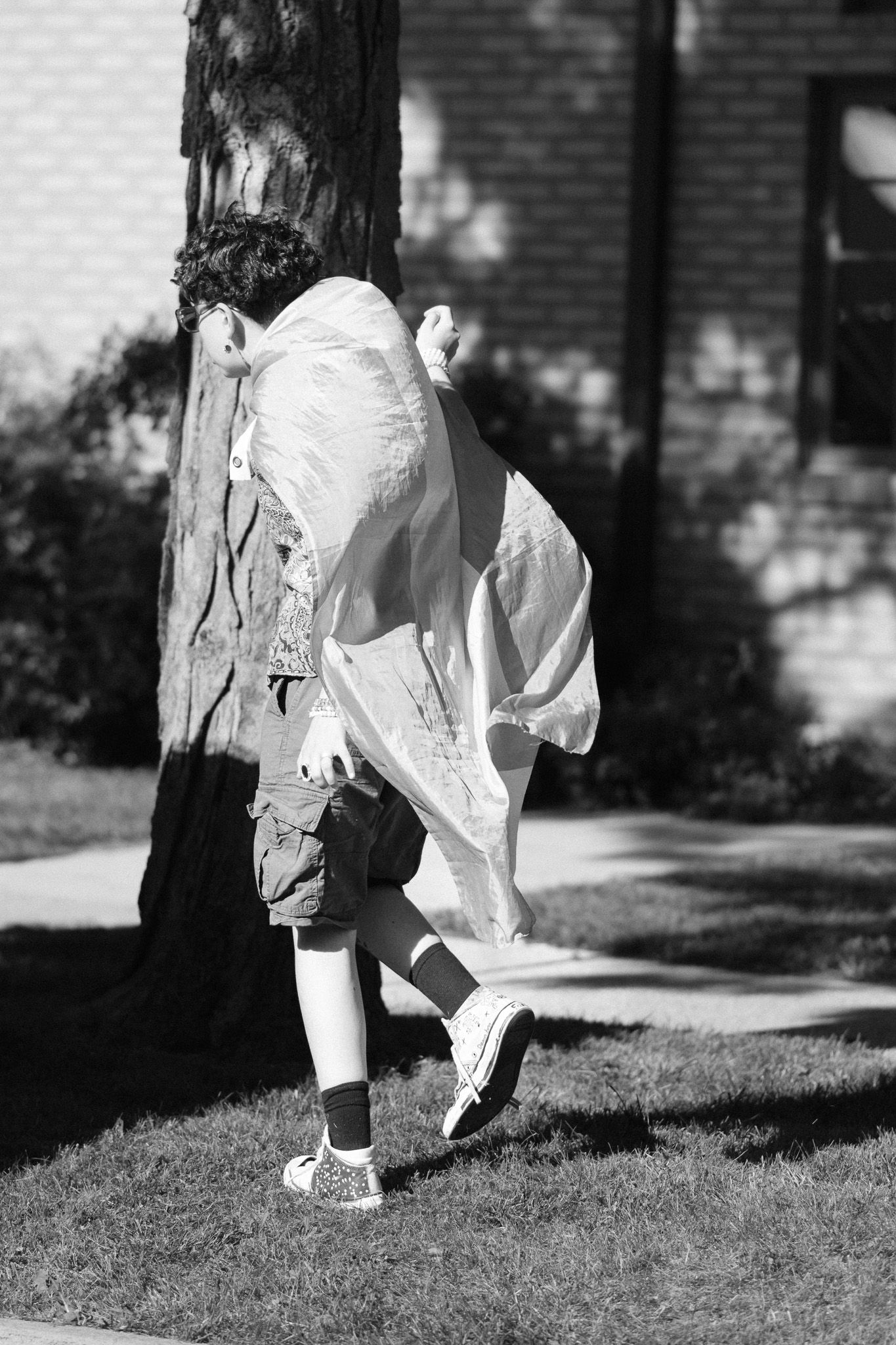 Black and white photo of someone in a flowing white dress running playfully past a tree.