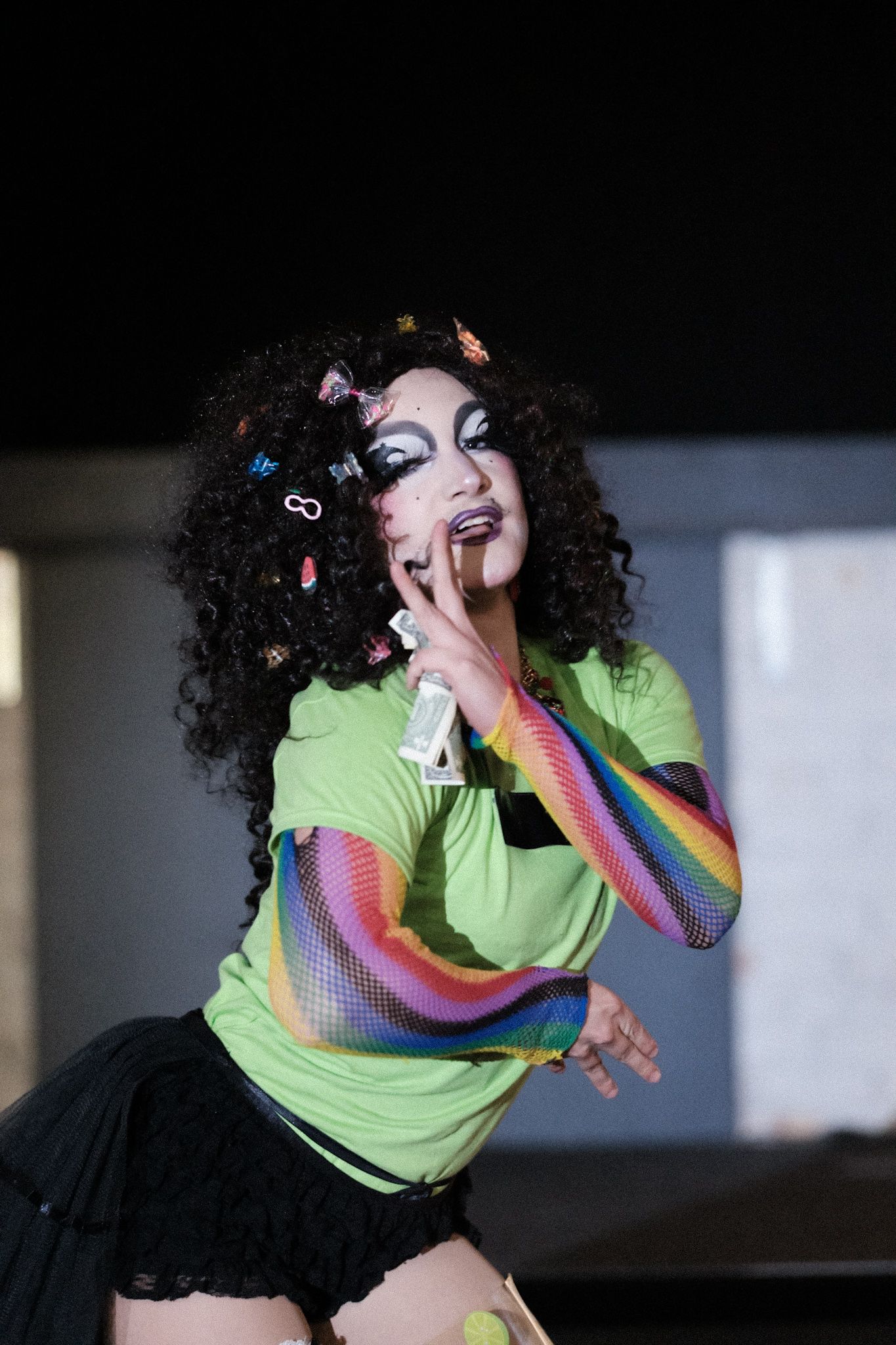 Performer in neon green top with rainbow sleeves and curly hair with butterflies.