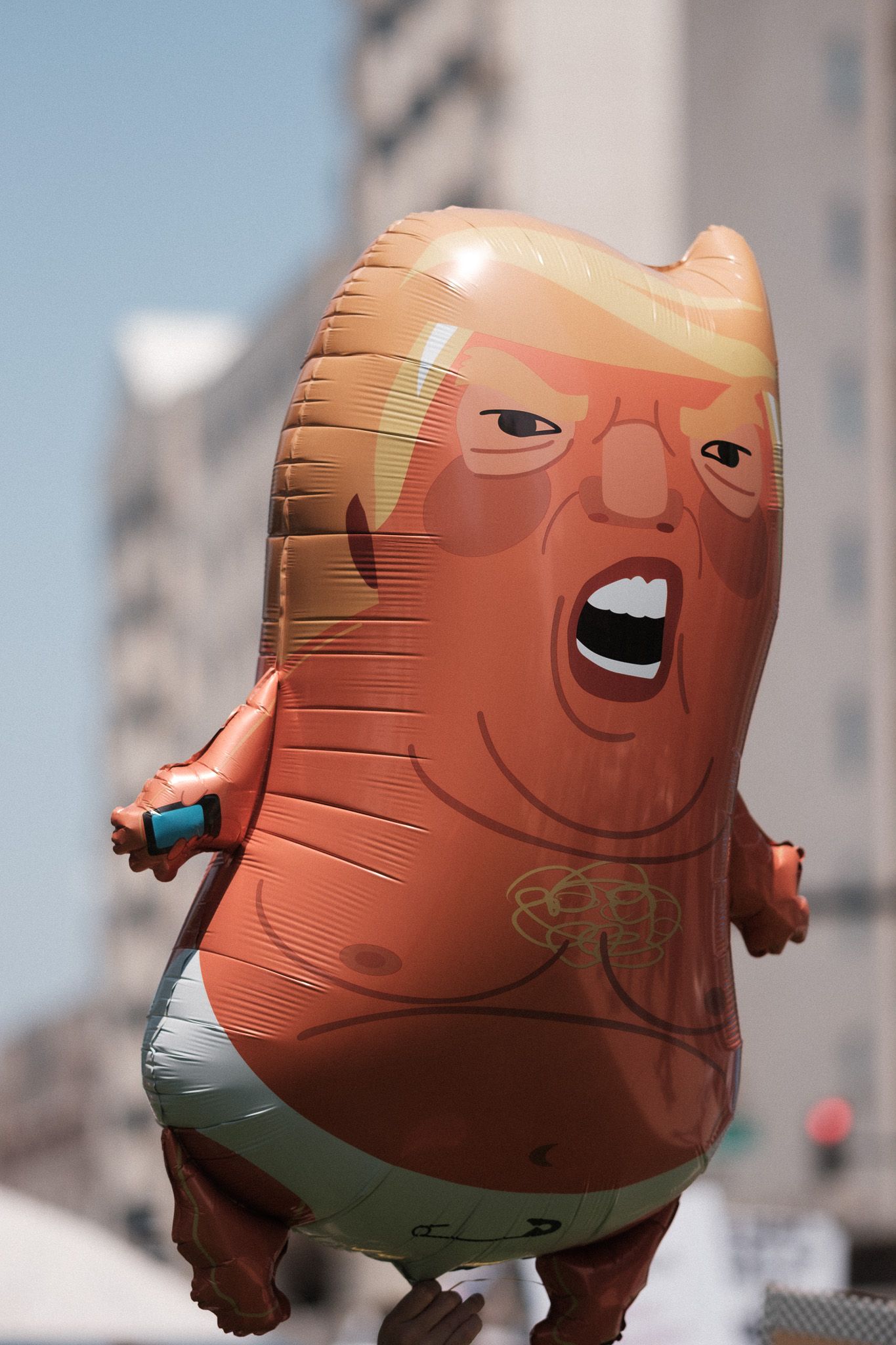 An inflatable caricature balloon floats above a protest crowd.