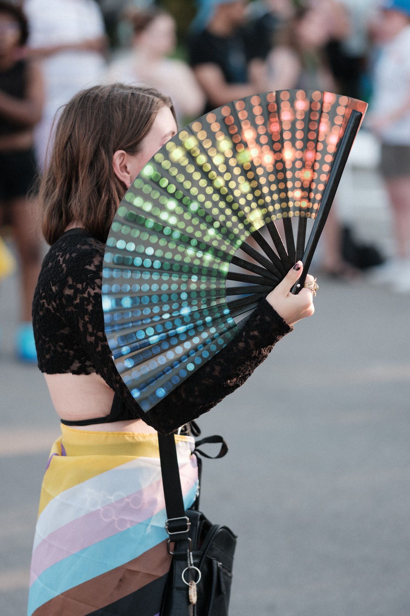 A colorful LED fan creates a dazzling light display at an outdoor festival against a blurred crowd background.