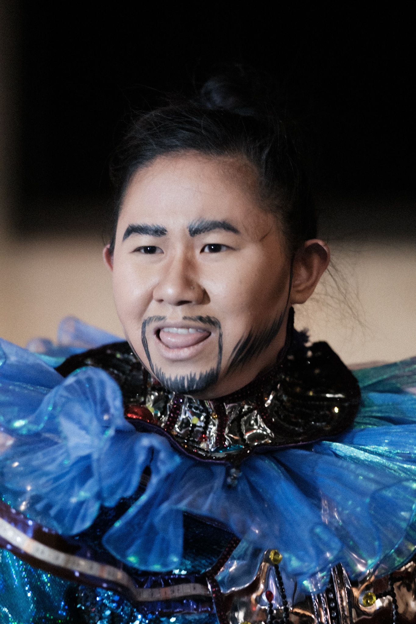 Theatrical performer in blue ruffled collar and dramatic stage makeup.