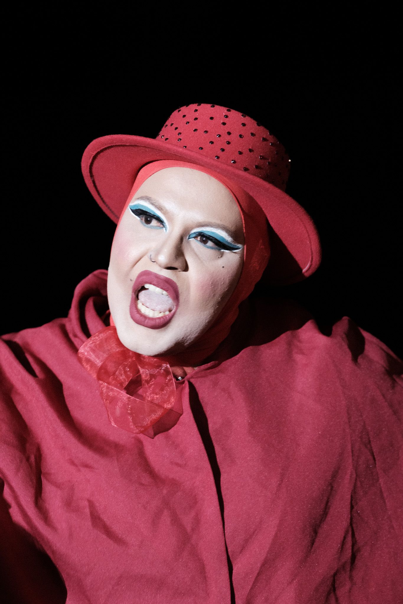 Dramatic stage performance featuring bright red hat and matching outfit with bold makeup.