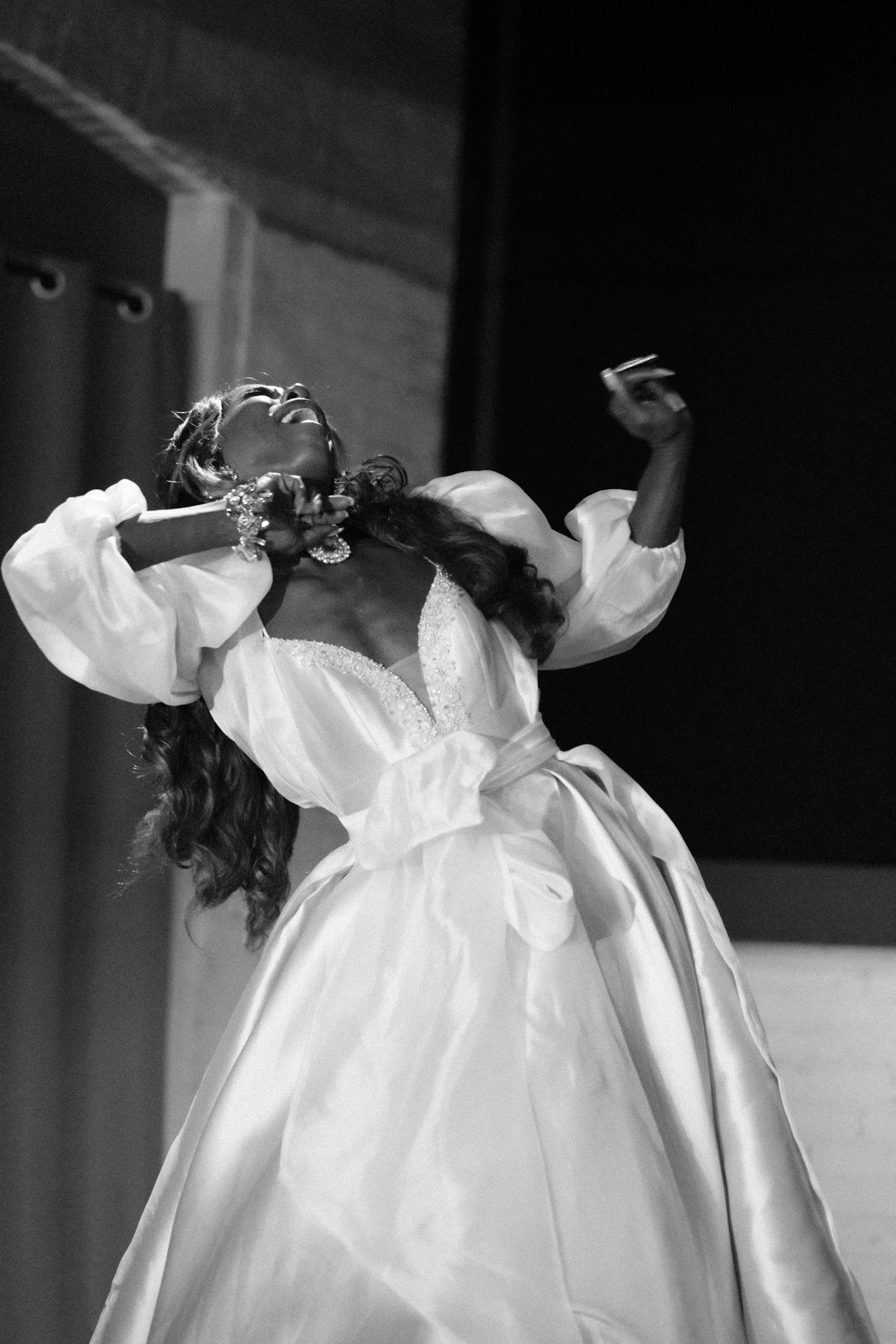 Performer in flowing white gown dancing expressively in black and white photograph.