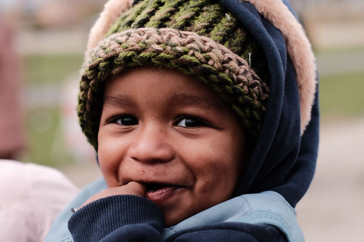 A smiling child wearing a knit beanie and winter coat enjoys a chilly outdoor day.