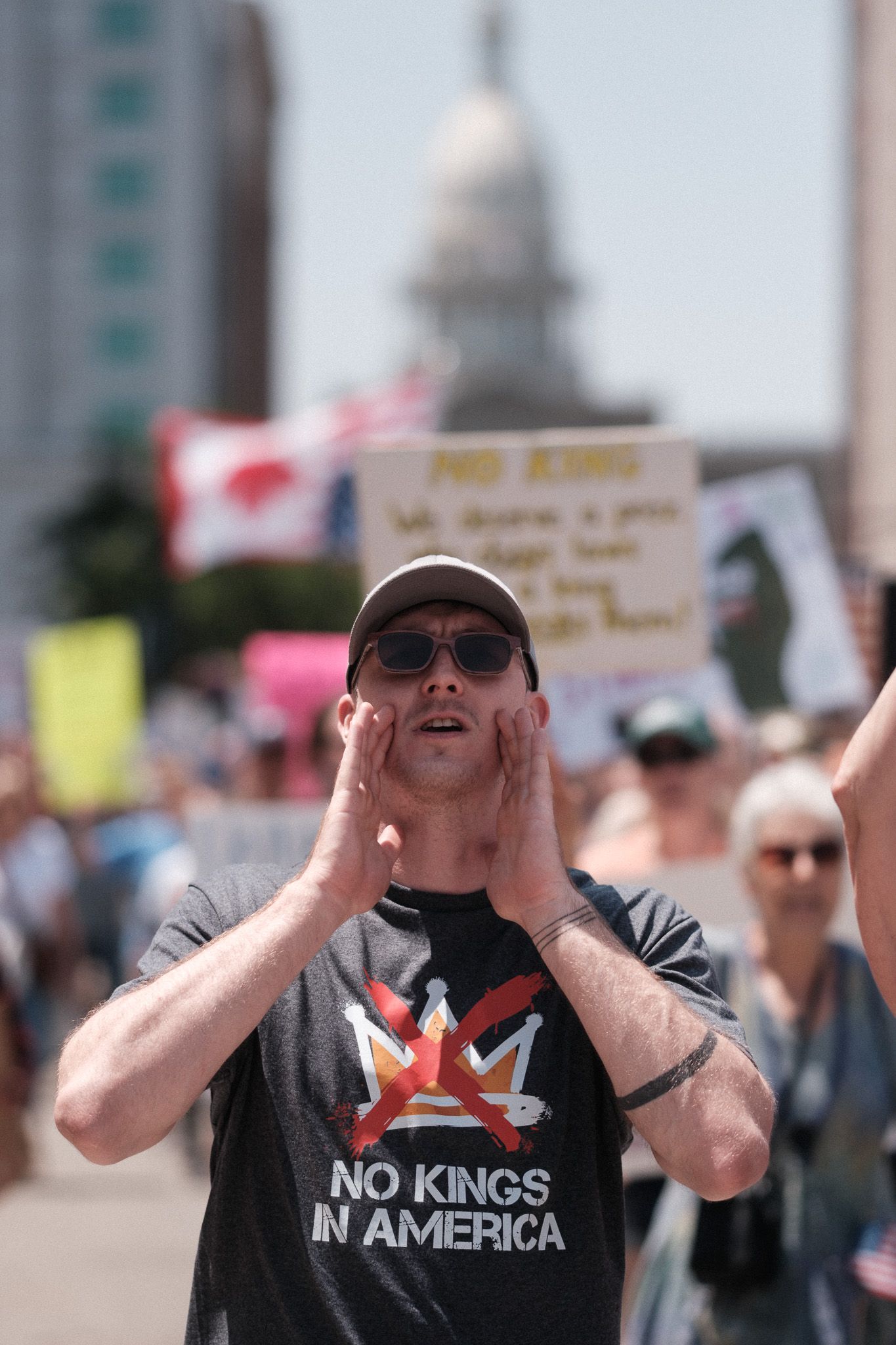 Protester shouts with hands cupped around mouth wearing a 'No Kings in America' t-shirt.
