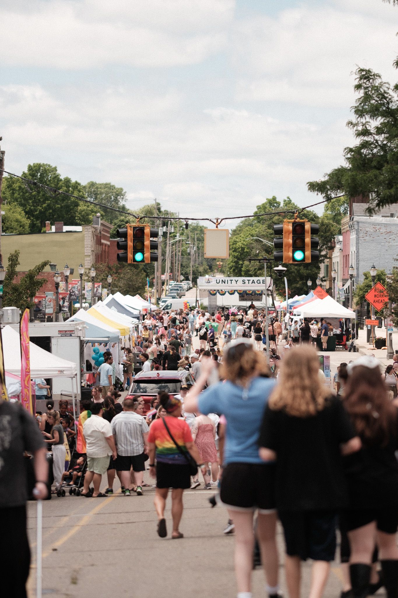 A crowded outdoor street festival with vendor tents and people walking along an urban street on a summer day.