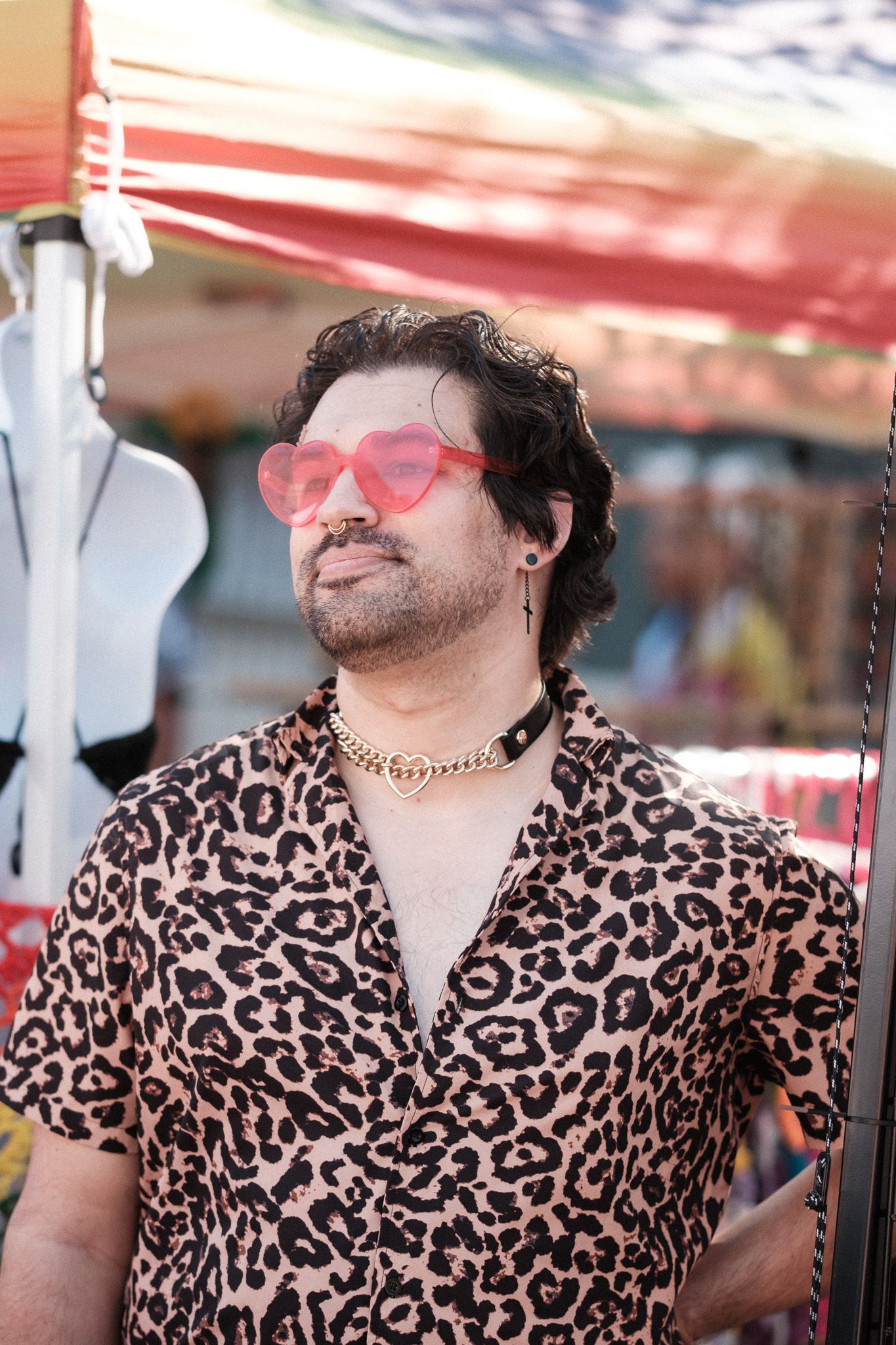 Person in leopard print shirt and heart-shaped pink sunglasses posing at an outdoor festival.