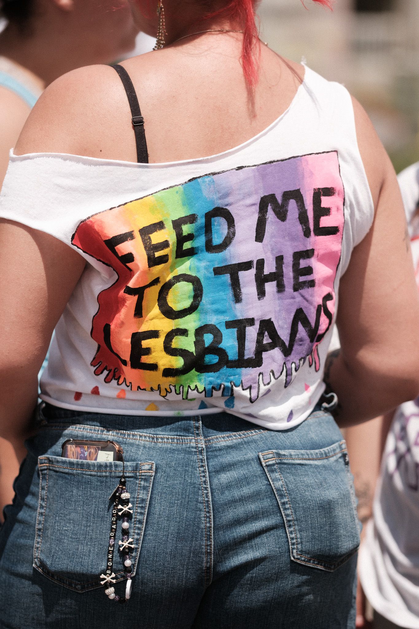 A rainbow tie-dye shirt with text 'FEED ME TO THE LESBIANS' worn with denim jeans.
