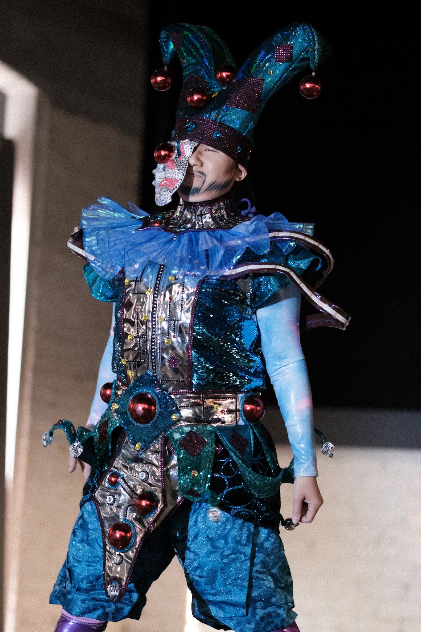 A performer wearing an elaborate blue and silver costume with a tall headdress and ornate decorative details on stage.