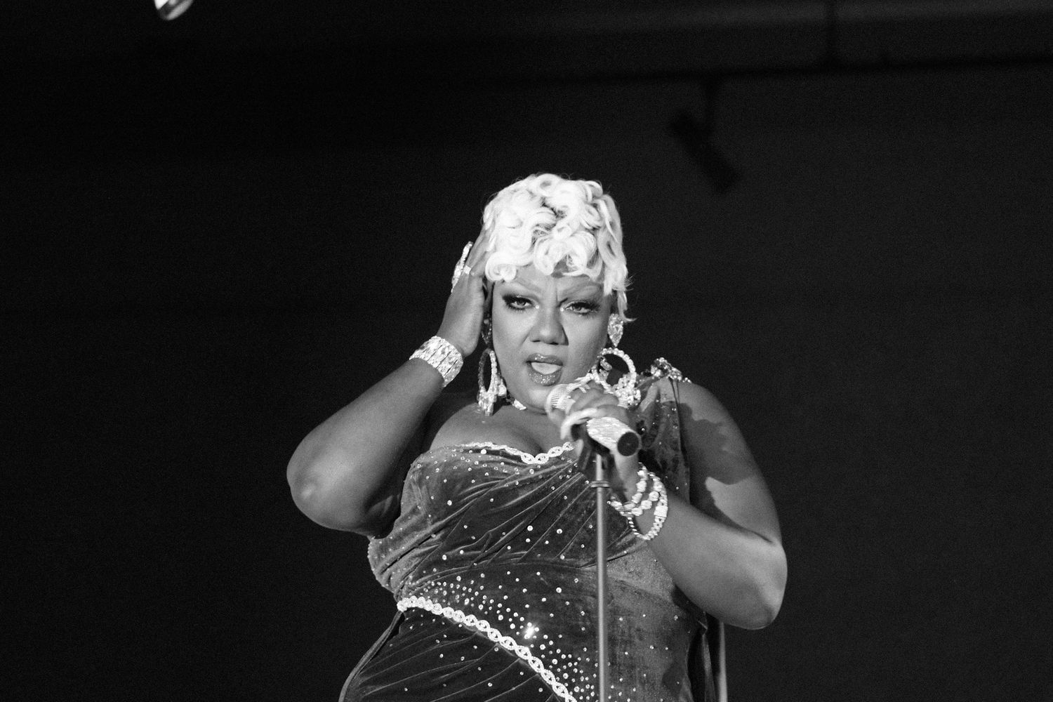 Performer in sparkly costume poses expressively during dramatic black and white stage performance.