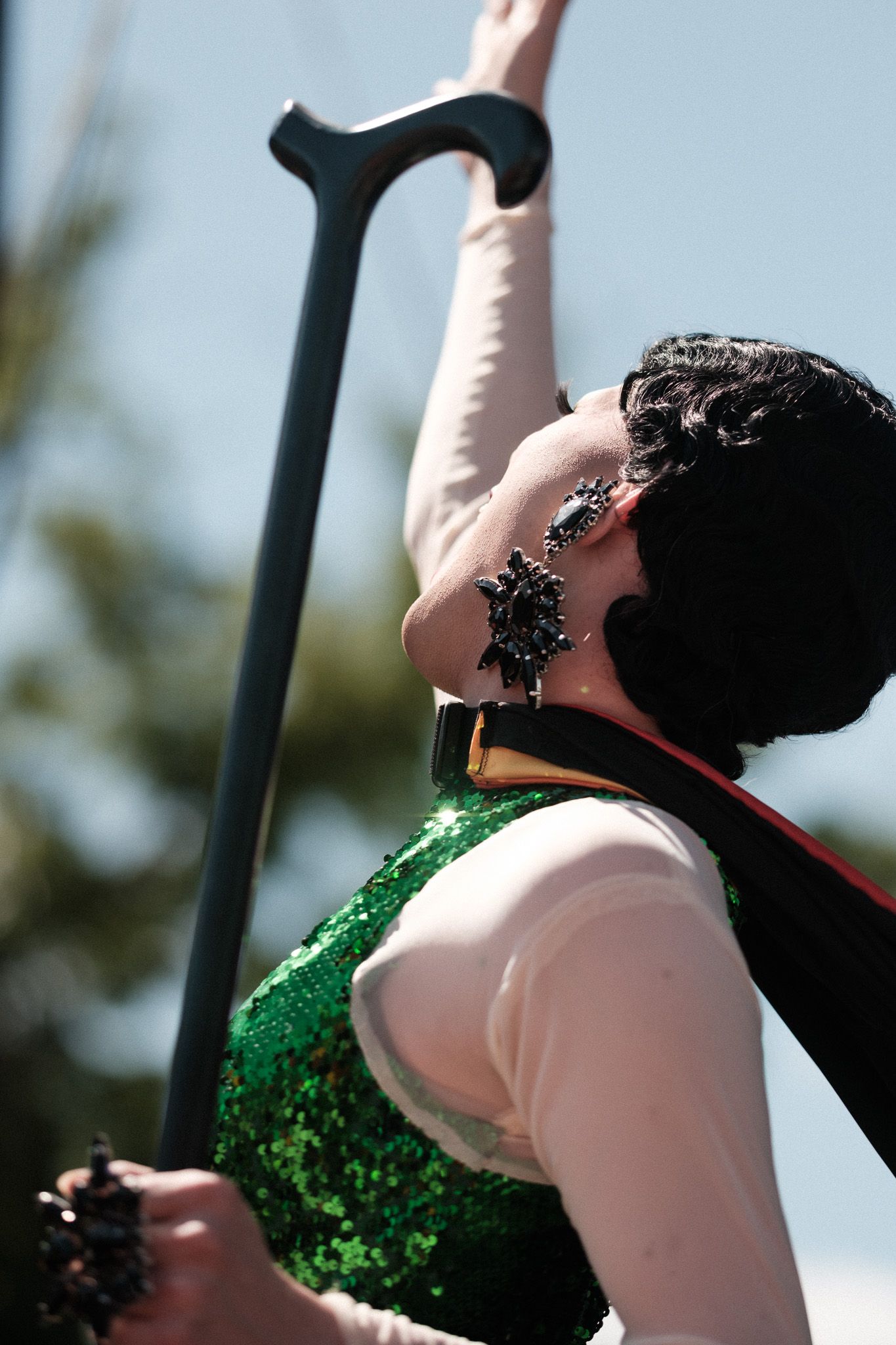 Side view of a performer in green sequin costume holding a black cane during a show.