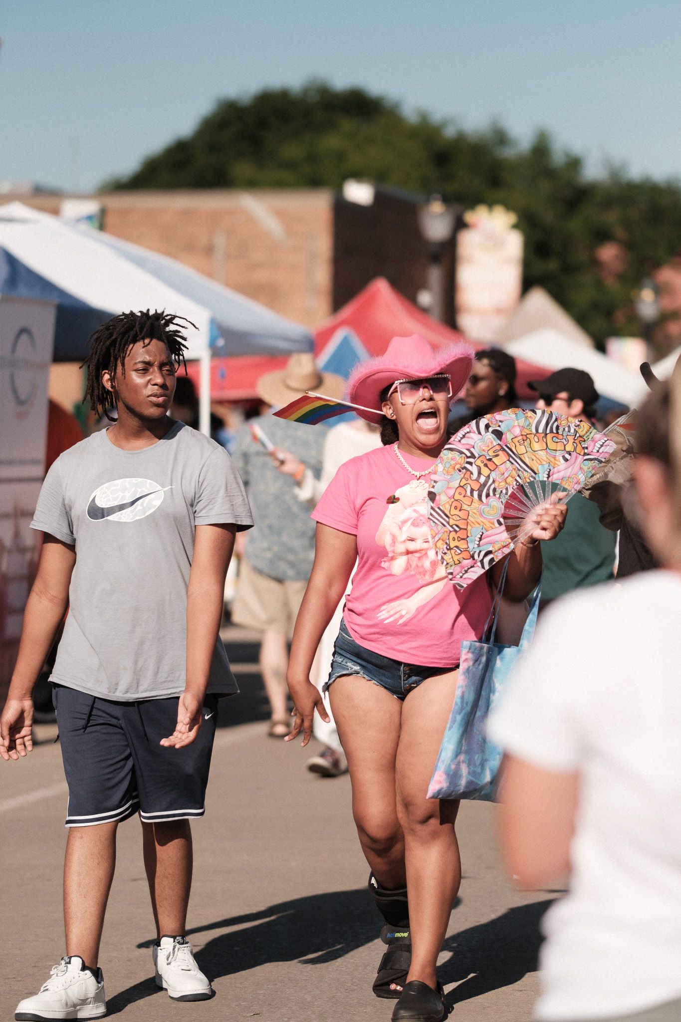 People walking through an outdoor festival marketplace with colorful tents in the background.
