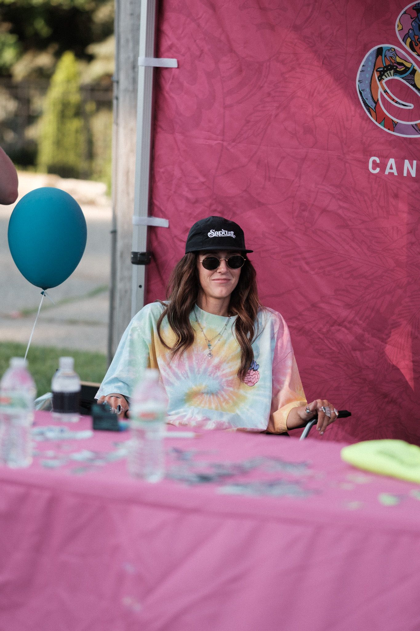 Festival booth setup with teal balloon and pink backdrop at outdoor event.