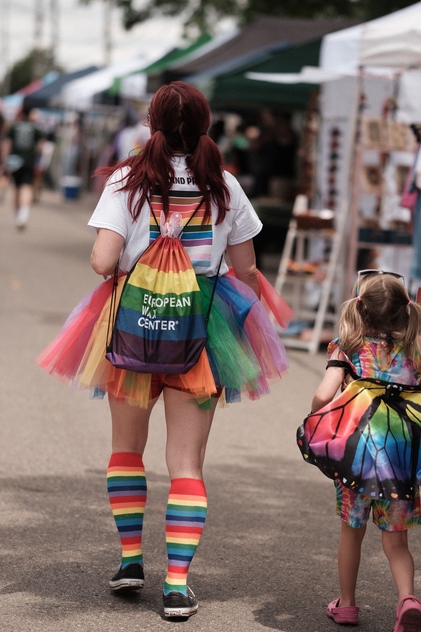 People wearing colorful rainbow tutus and striped socks walking at an outdoor event.