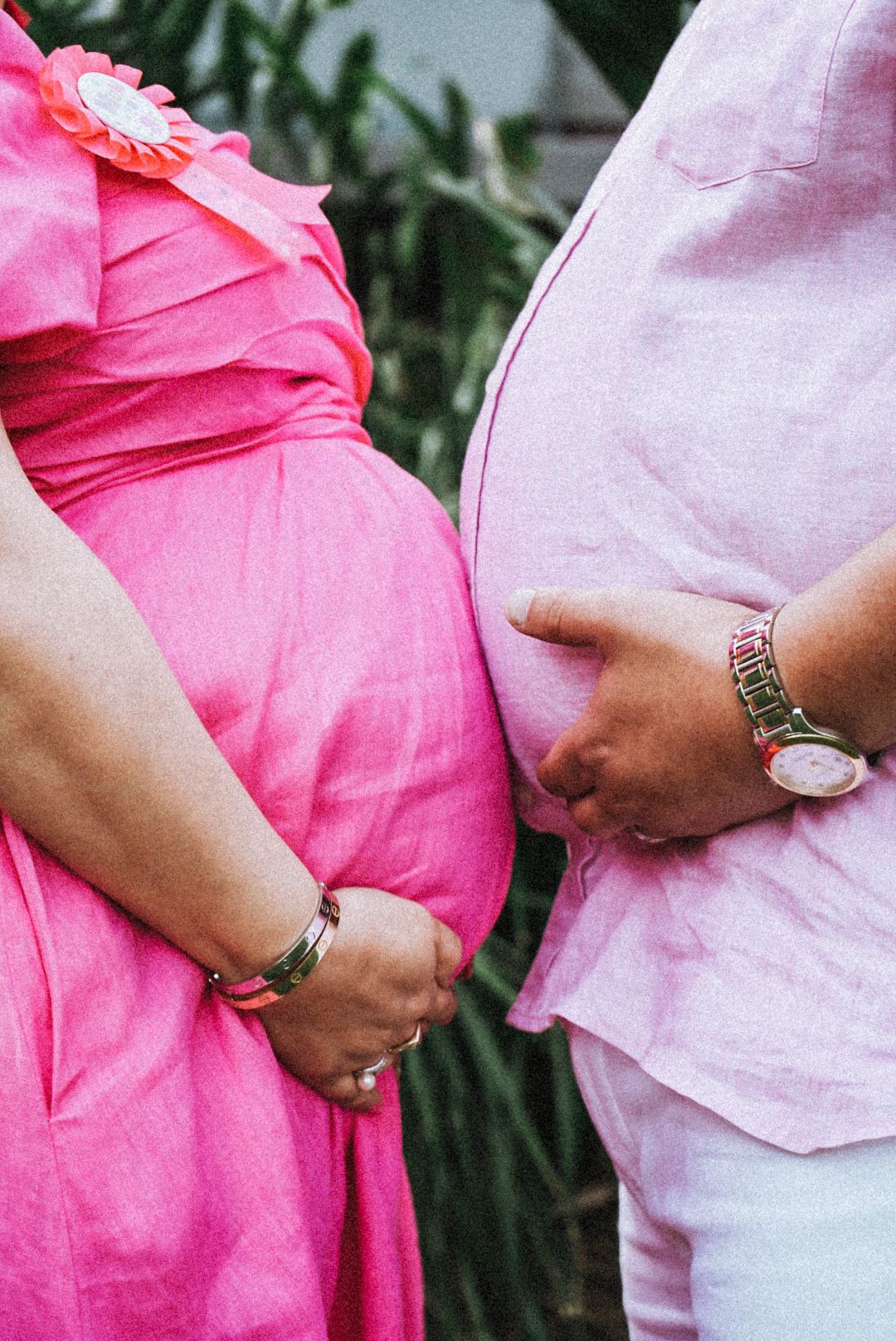 Close-up of hands resting on a pregnant belly wearing pink clothing.