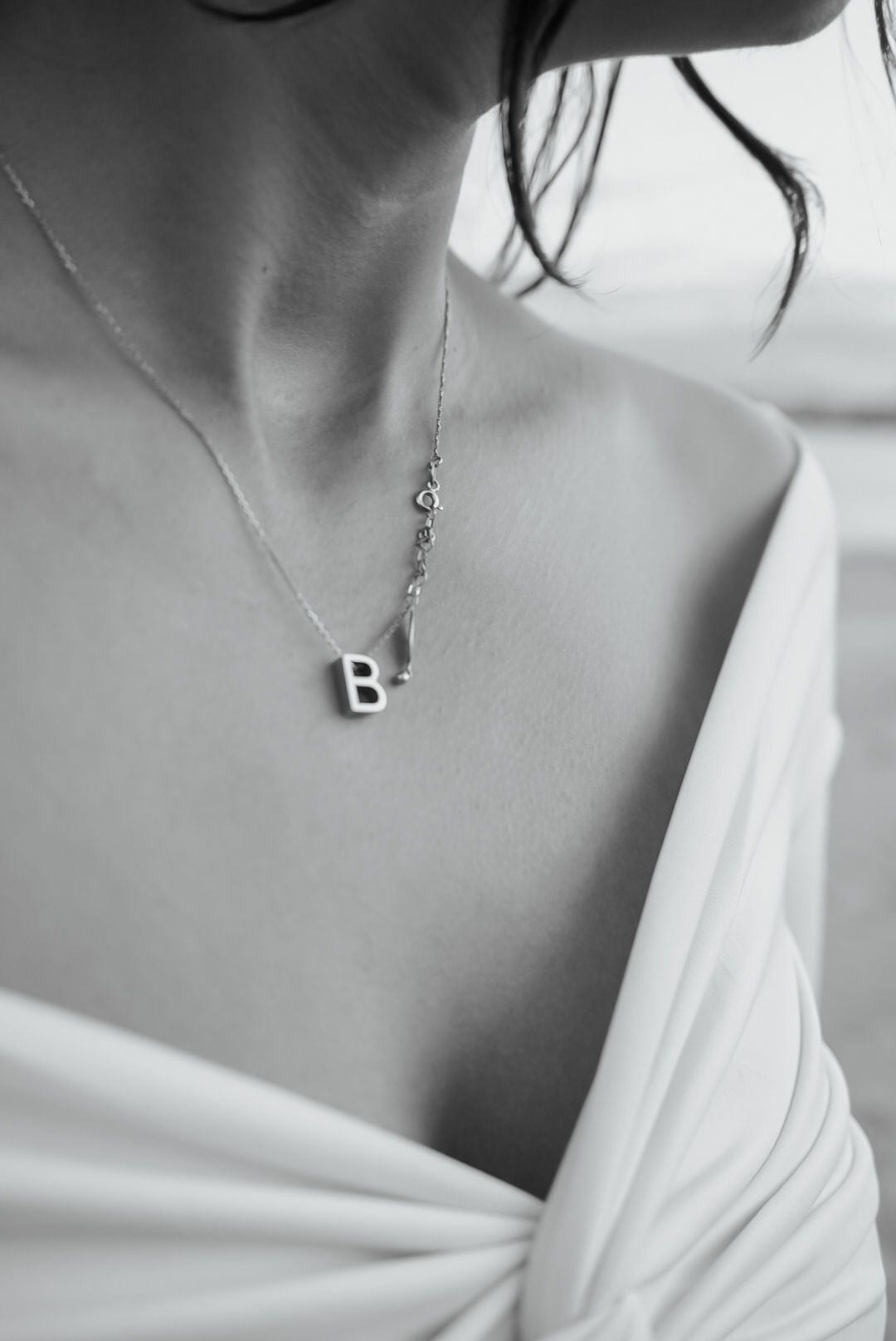 Close-up black and white shot showing a delicate necklace with letter pendant.