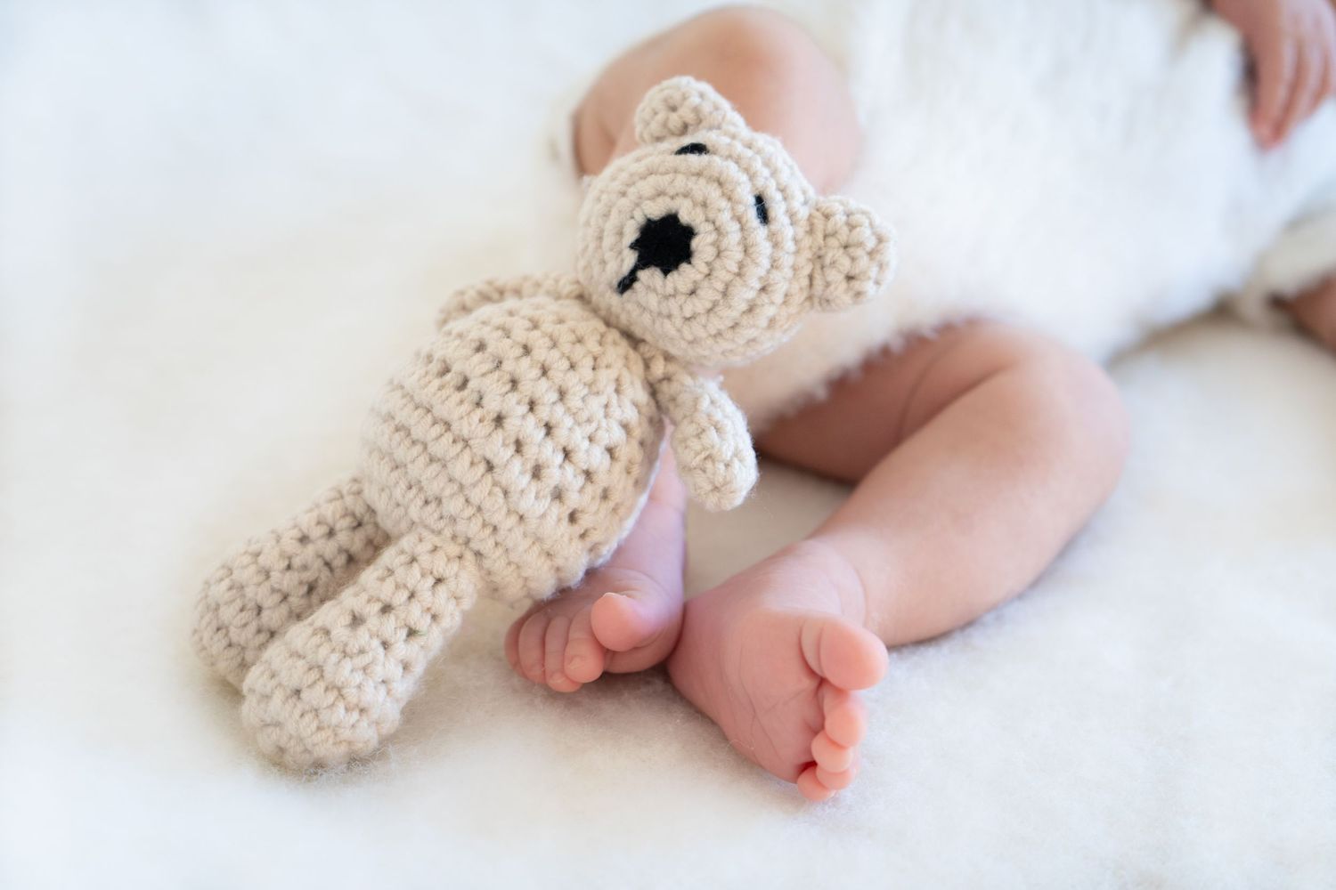 Tiny baby feet wearing soft knitted beige bunny slippers with adorable bow details.