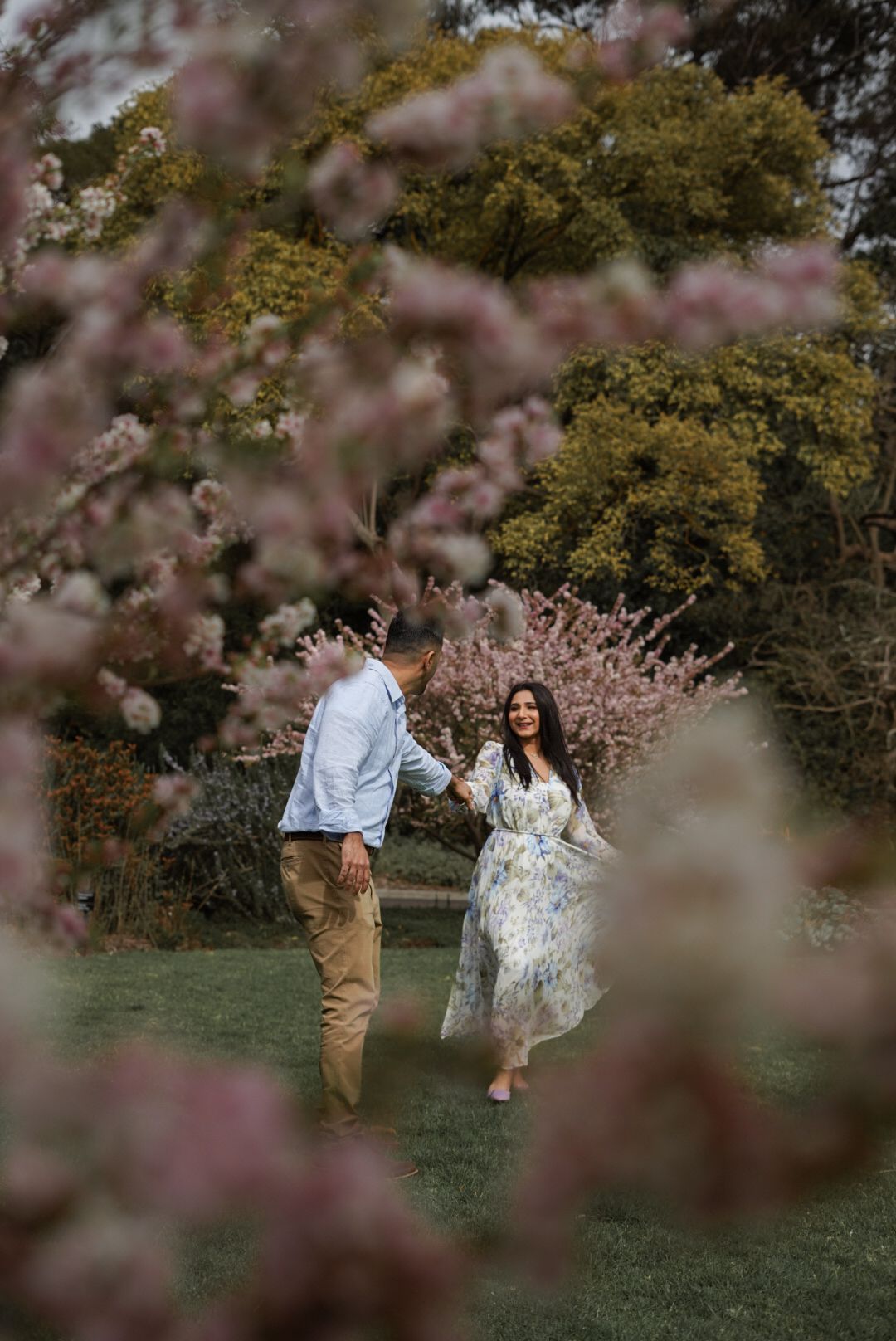 Couple dances joyfully under blooming cherry blossom trees in spring.