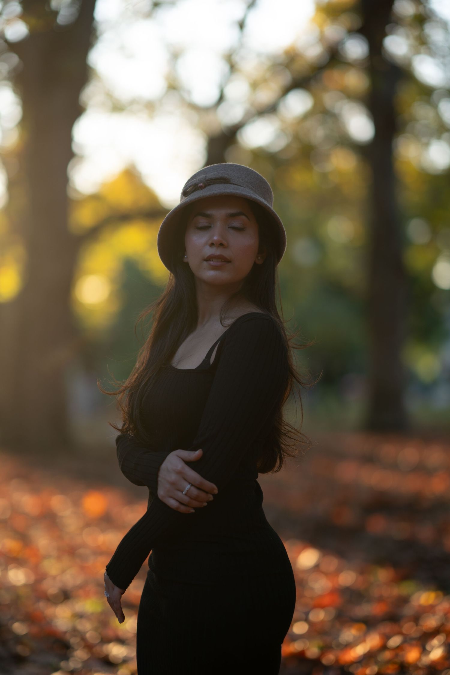 Person in black outfit dances among autumn leaves in golden sunlight.