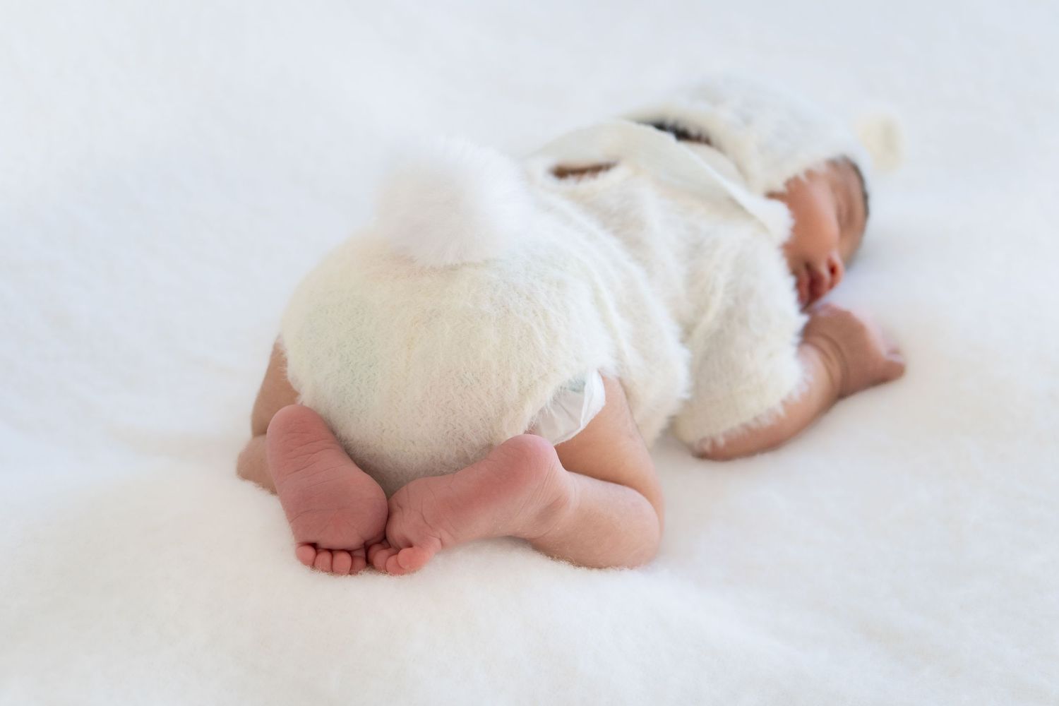 Tiny bare feet of a sleeping baby wrapped in white blanket on light background.