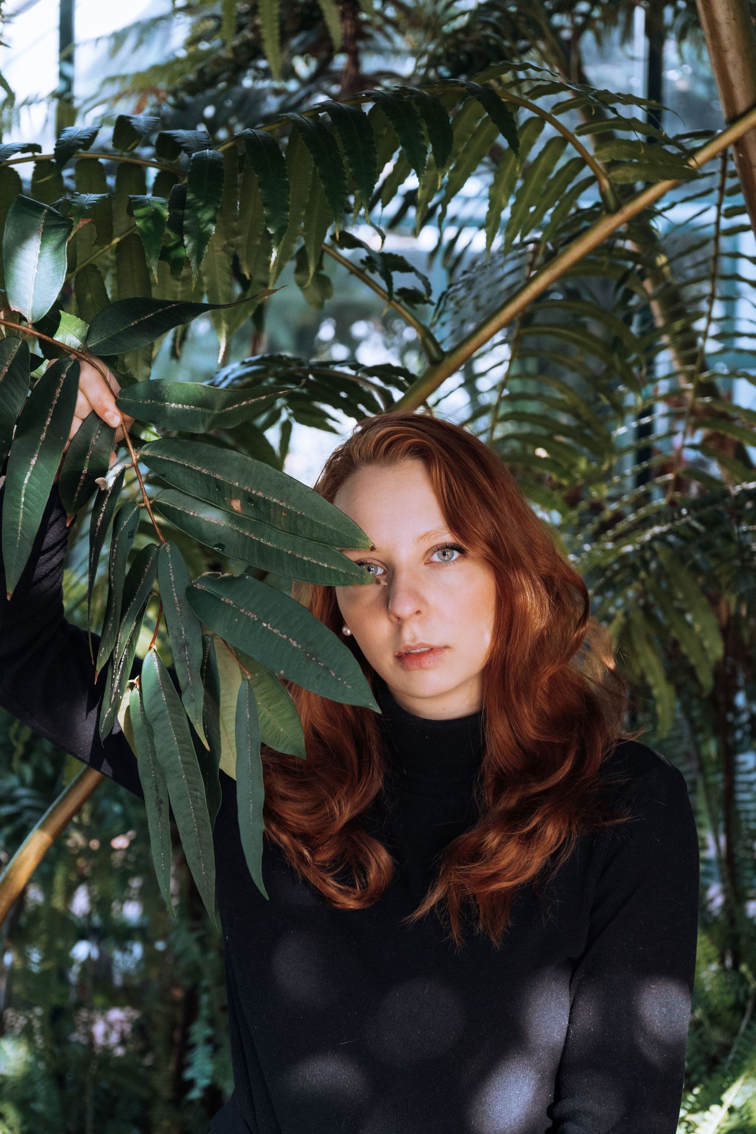 Person with auburn hair poses among tropical plants and monstera leaves.