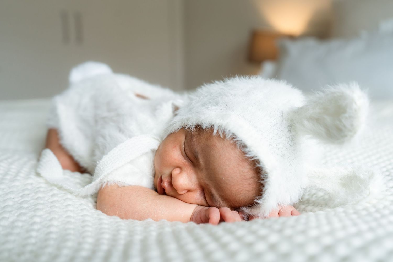 A newborn baby sleeping peacefully on soft white textured blankets in natural light.