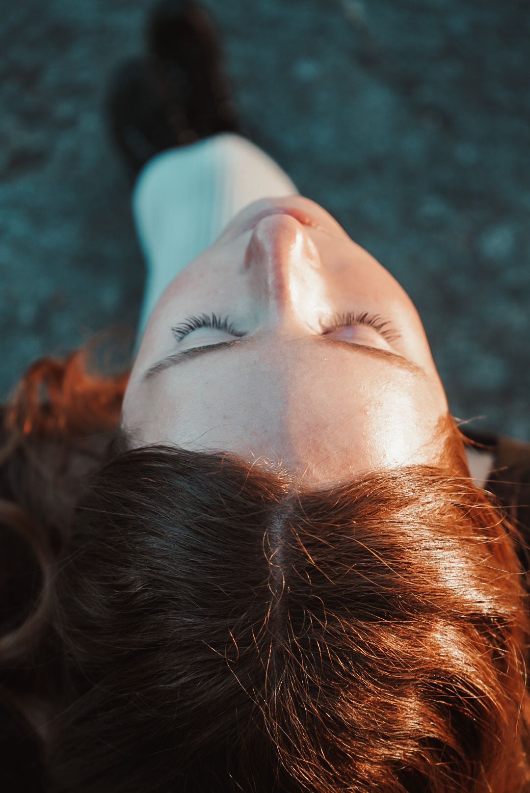 Artistic beauty portrait showing closed eyes and auburn hair against dark background.