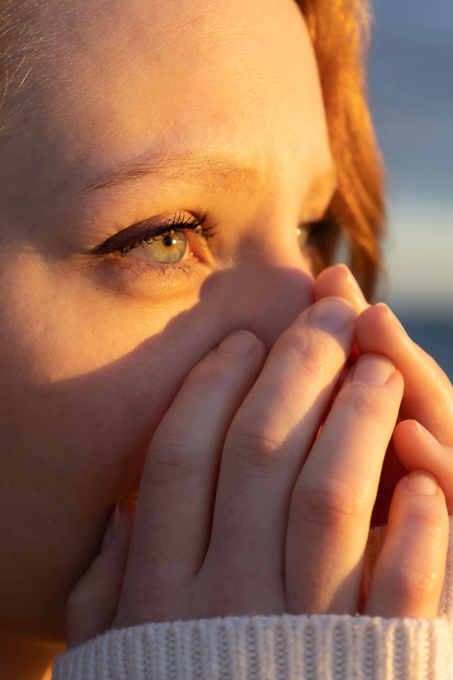 Close-up of hands covering face in soft natural lighting.
