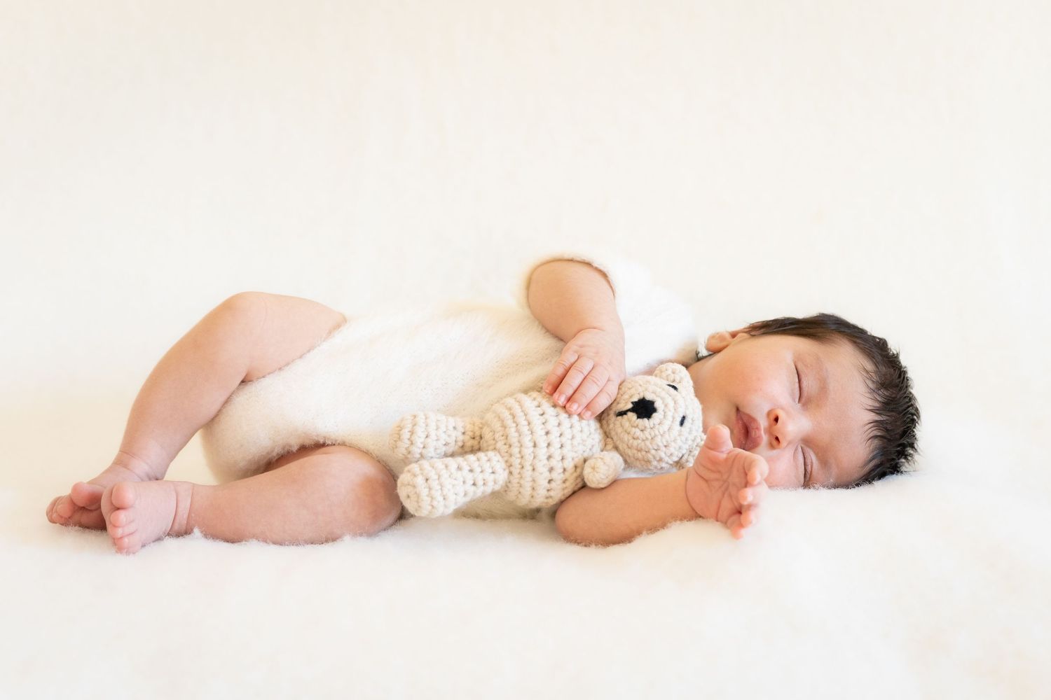 Baby wearing white diaper lying on side against white background in studio setting.