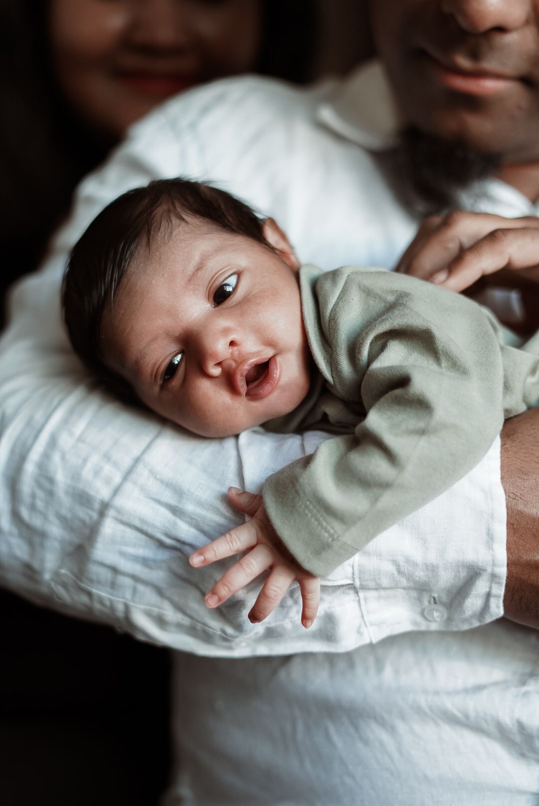 Close-up portrait of alert infant in gray onesie lying on white pillow.
