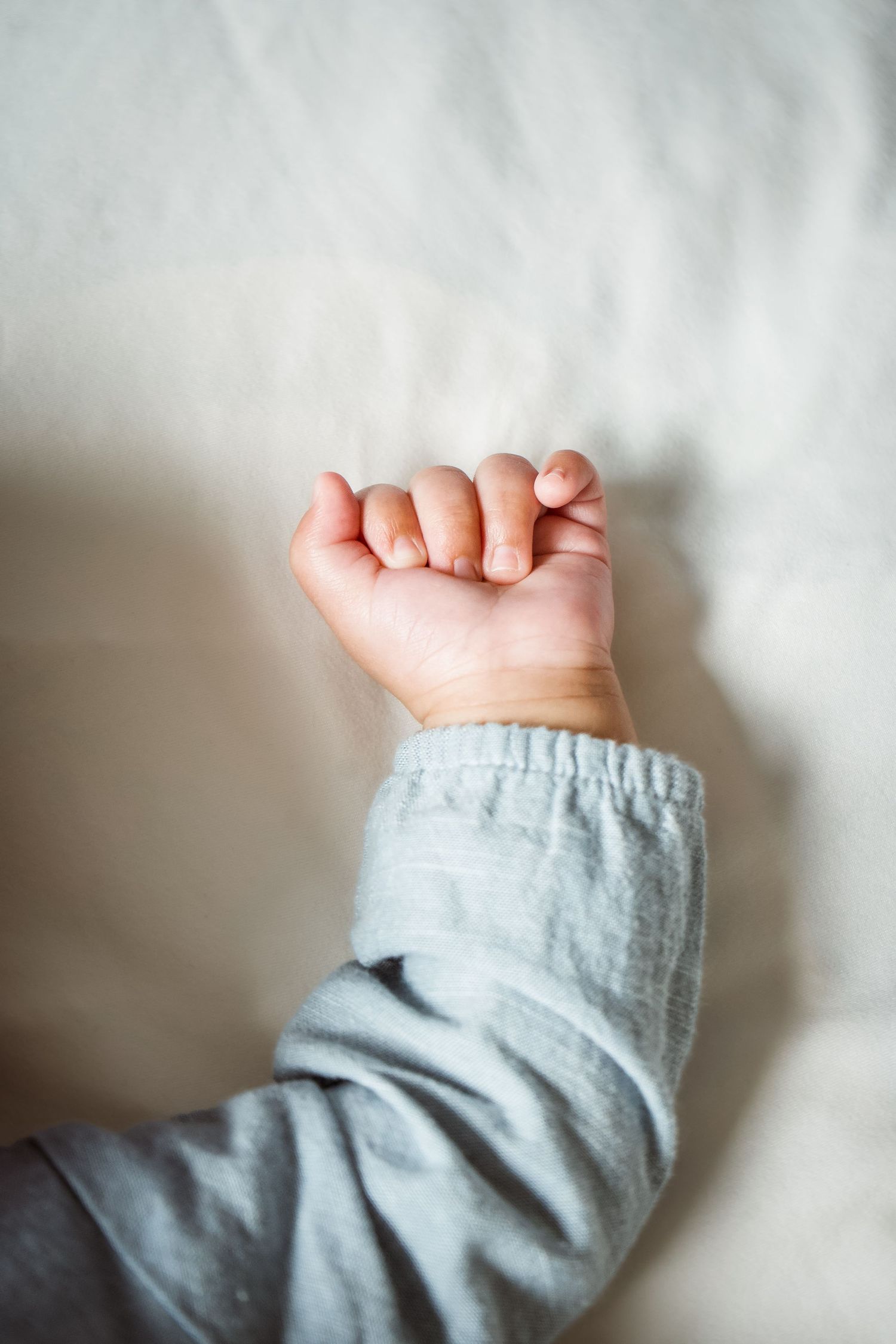 A series of close-up photos showing a baby's tiny hand and arm wearing a soft gray sleeve against a white background.