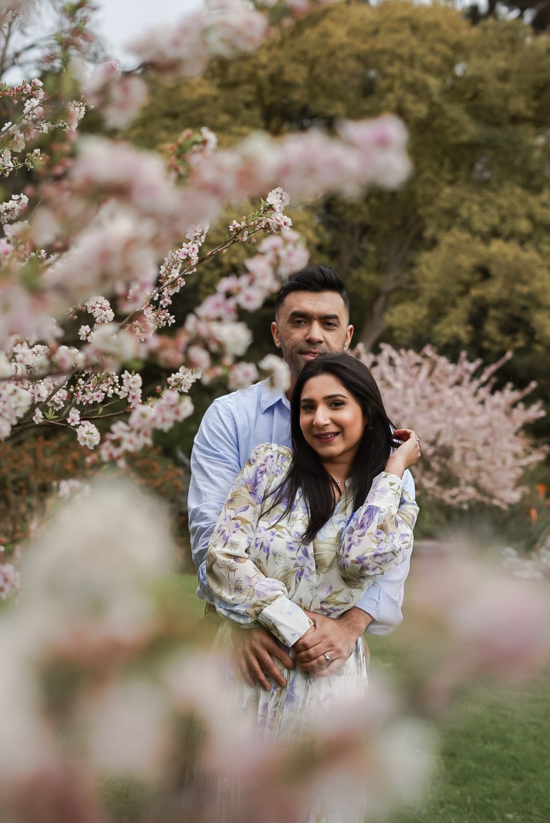 Romantic engagement photo with cherry blossoms blooming in background.