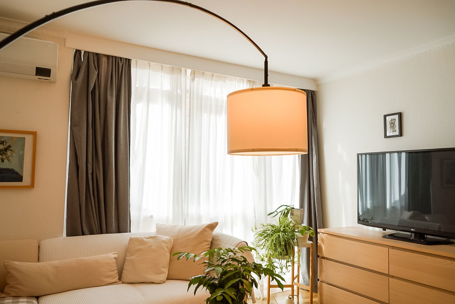 Modern living room with arched floor lamp and brown curtains near a TV setup.