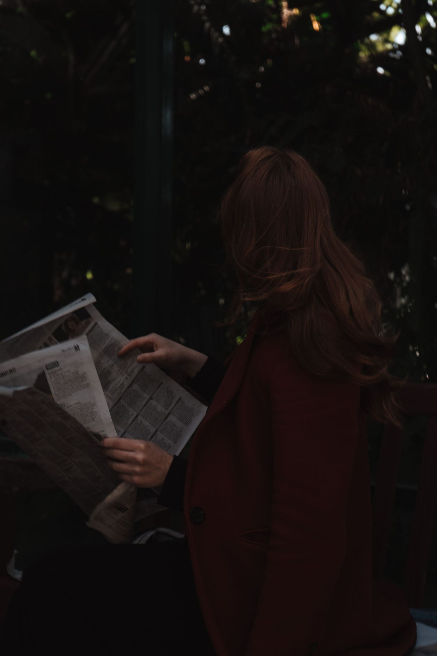 Silhouette of someone reading a newspaper in dim lighting.