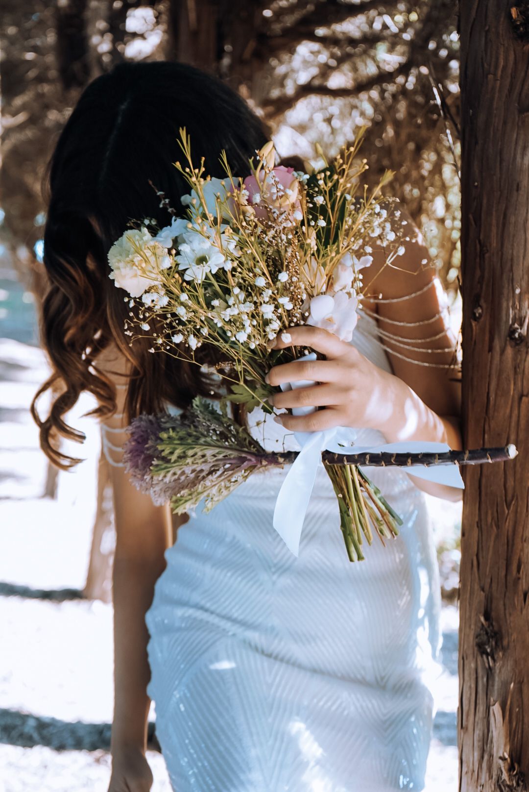 Person in white dress holding a delicate wildflower bouquet in a snowy forest setting.