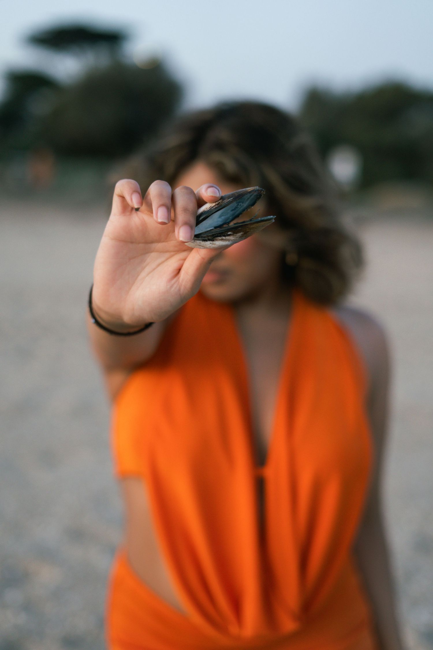 Figure in bright orange clothing poses expressively against a blurred outdoor background.