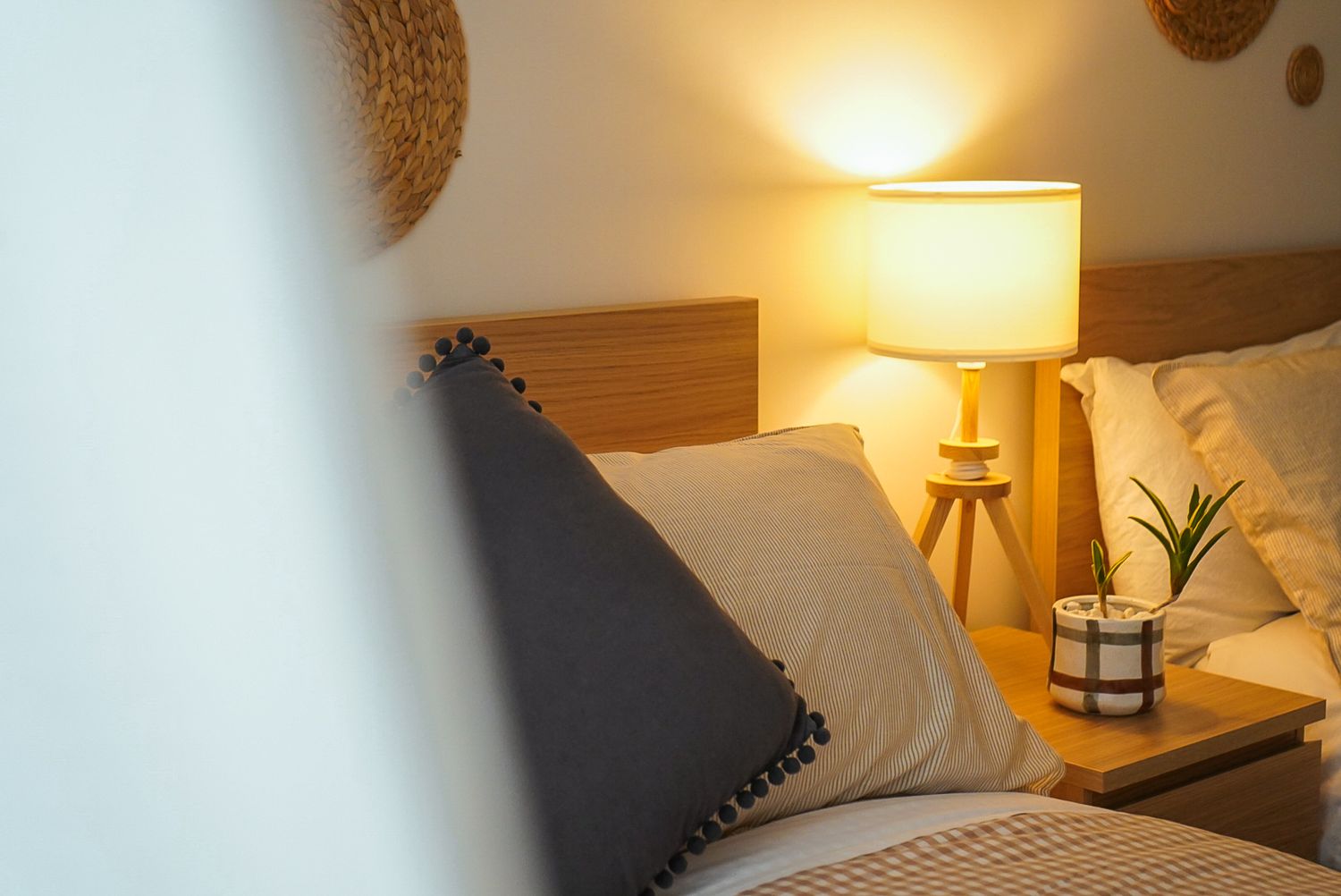 A cozy bedroom corner with a wooden nightstand, table lamp, and decorative pillows.