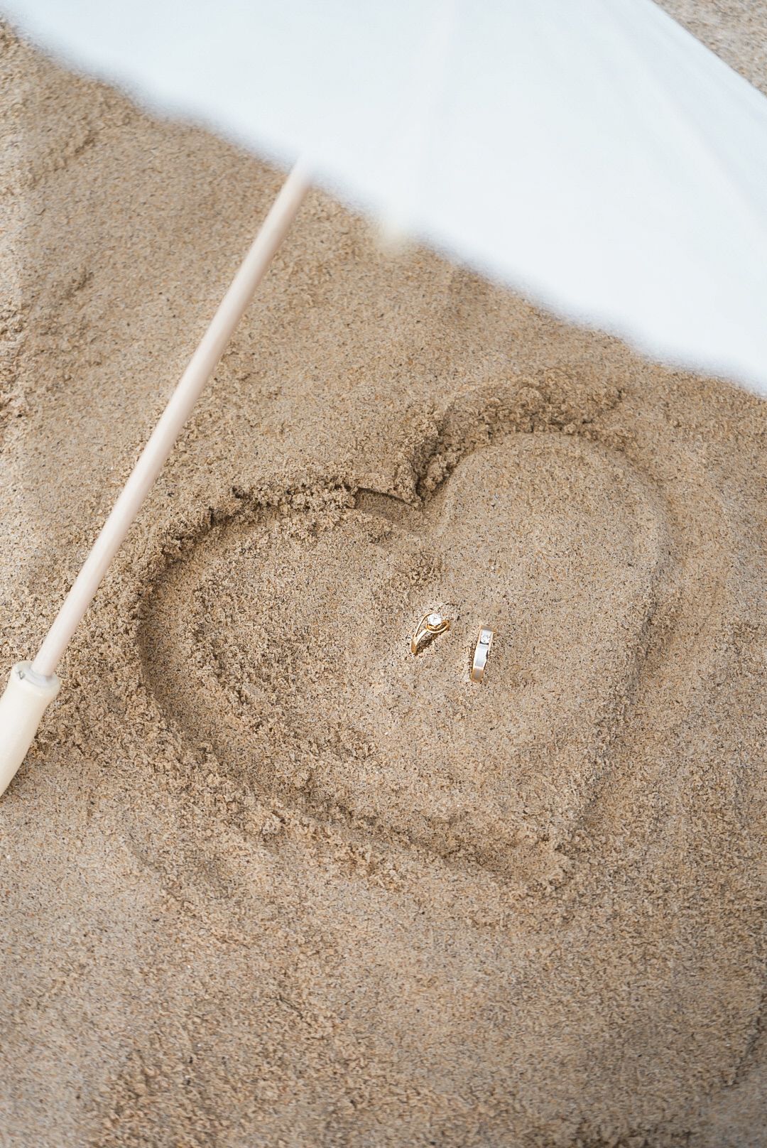 A heart shape drawn in smooth sand with sunlight casting a diagonal shadow across the beach.