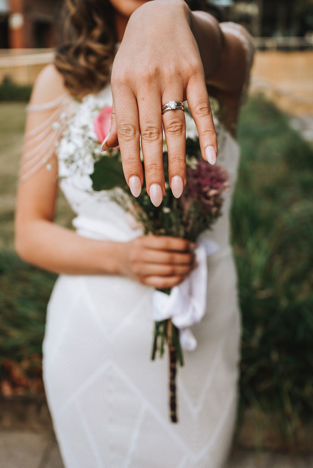 Close-up of hands holding a rustic wedding bouquet with painted nails and an engagement ring.