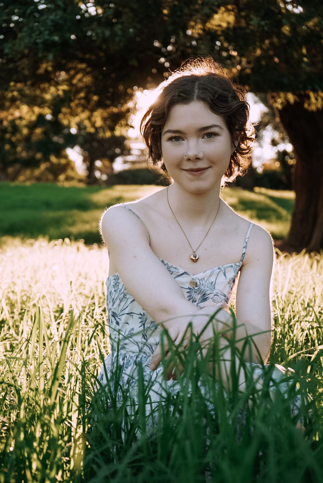 Person in floral dress sitting among tall grass at golden hour.