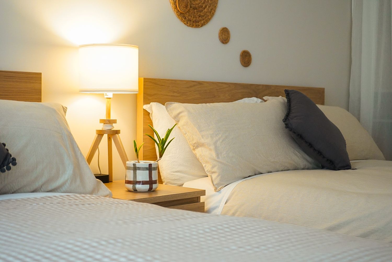 Cozy bedroom interior with white bedding, wooden headboard, and warm lamp lighting on nightstand.