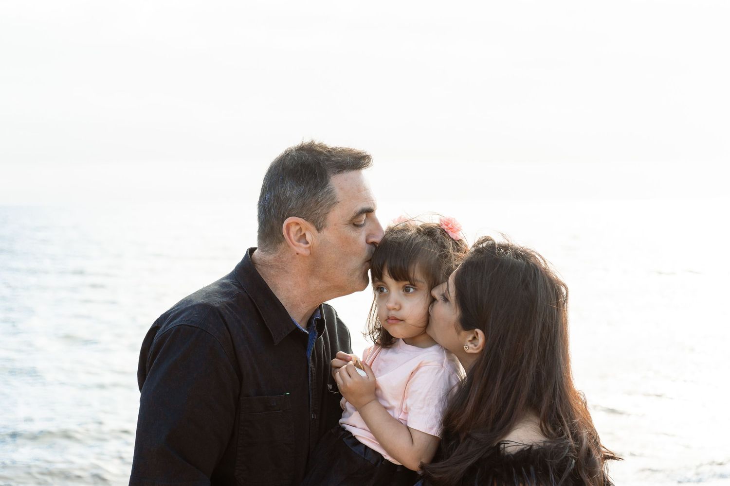 A loving family shares a tender moment together by the ocean at sunset.