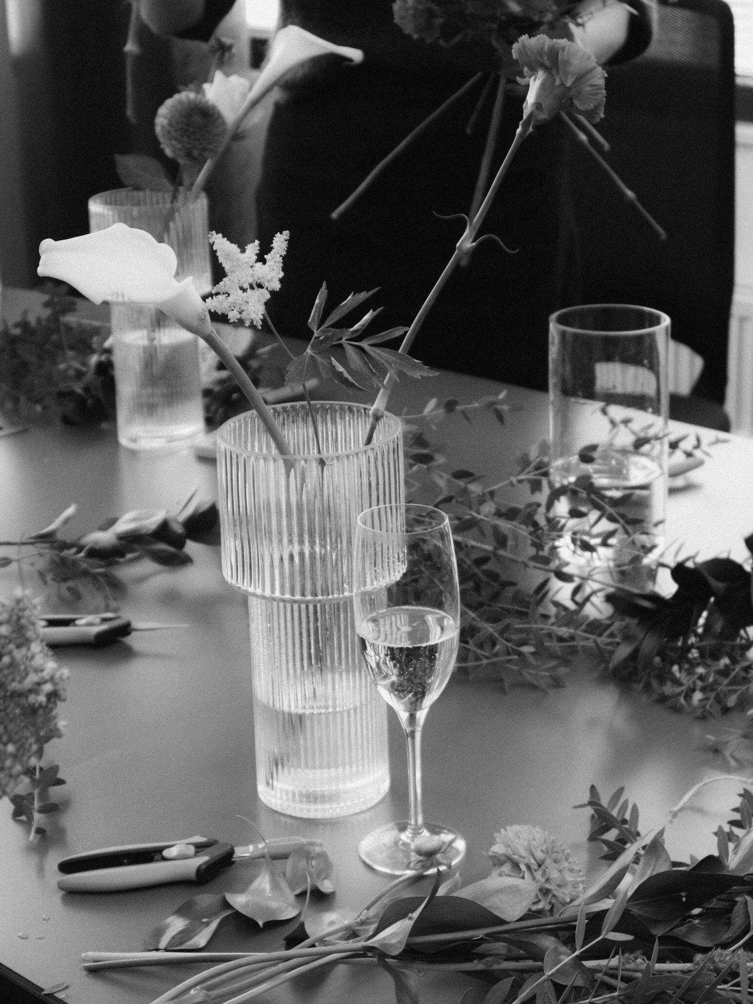 Black and white photo of wine glasses and decorative vases arranged on a table with floral elements and leaves.