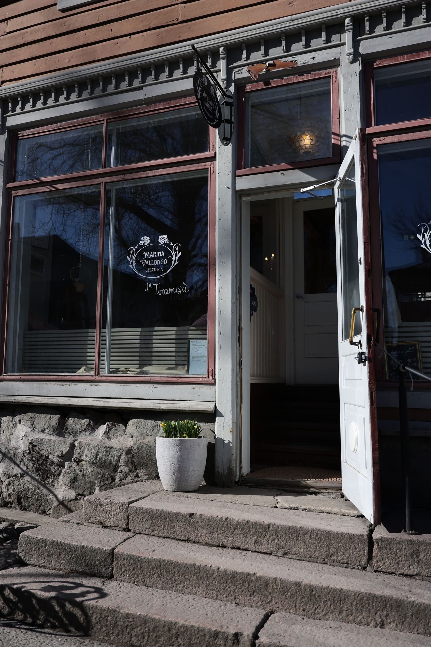 Stone steps lead up to a row of storefront windows with black awnings and white pillars along a commercial building exterior.