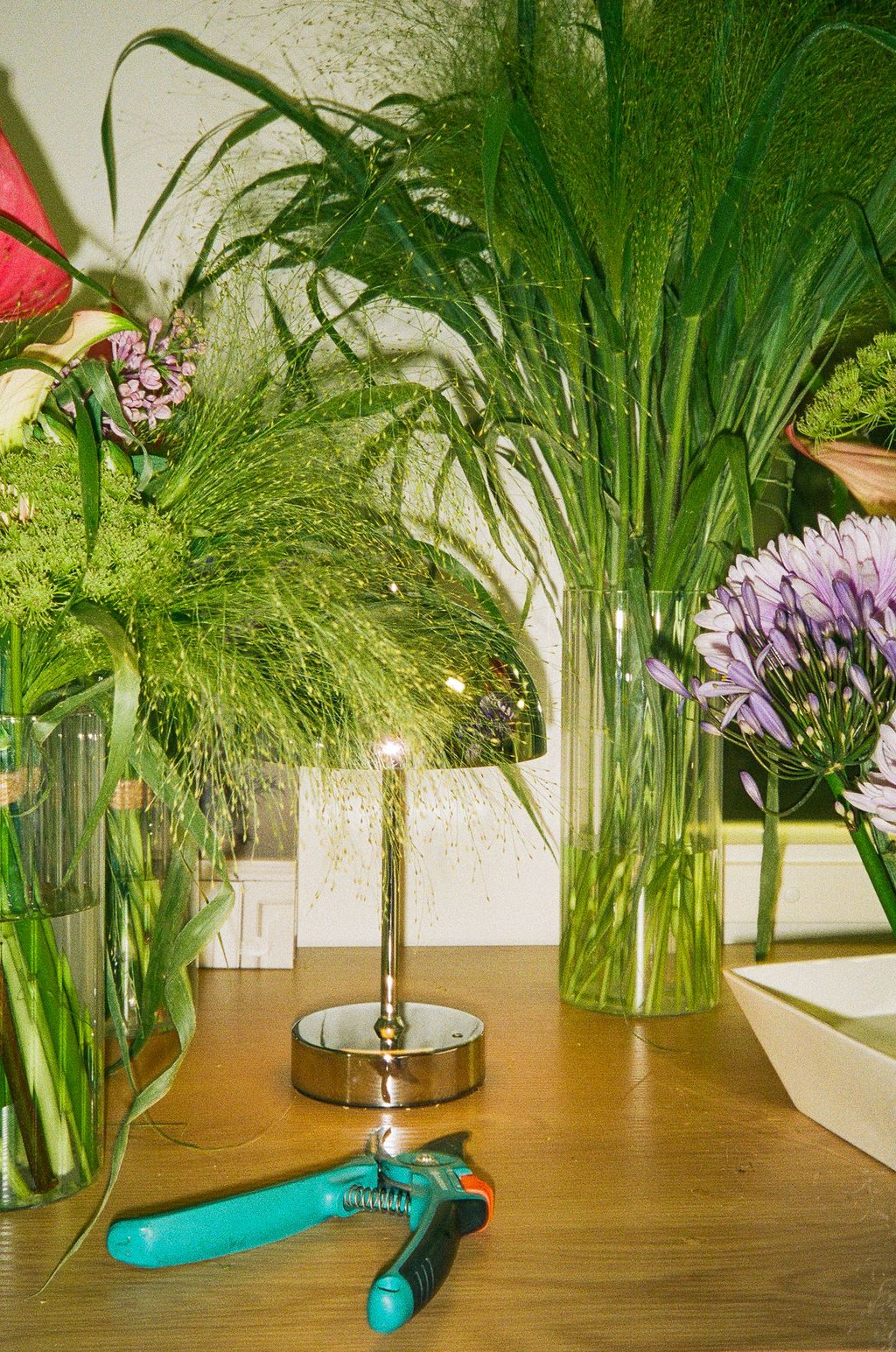 Five glass vases with fresh cut flowers arranged in a row on a wooden table display colorful blooms and greenery.