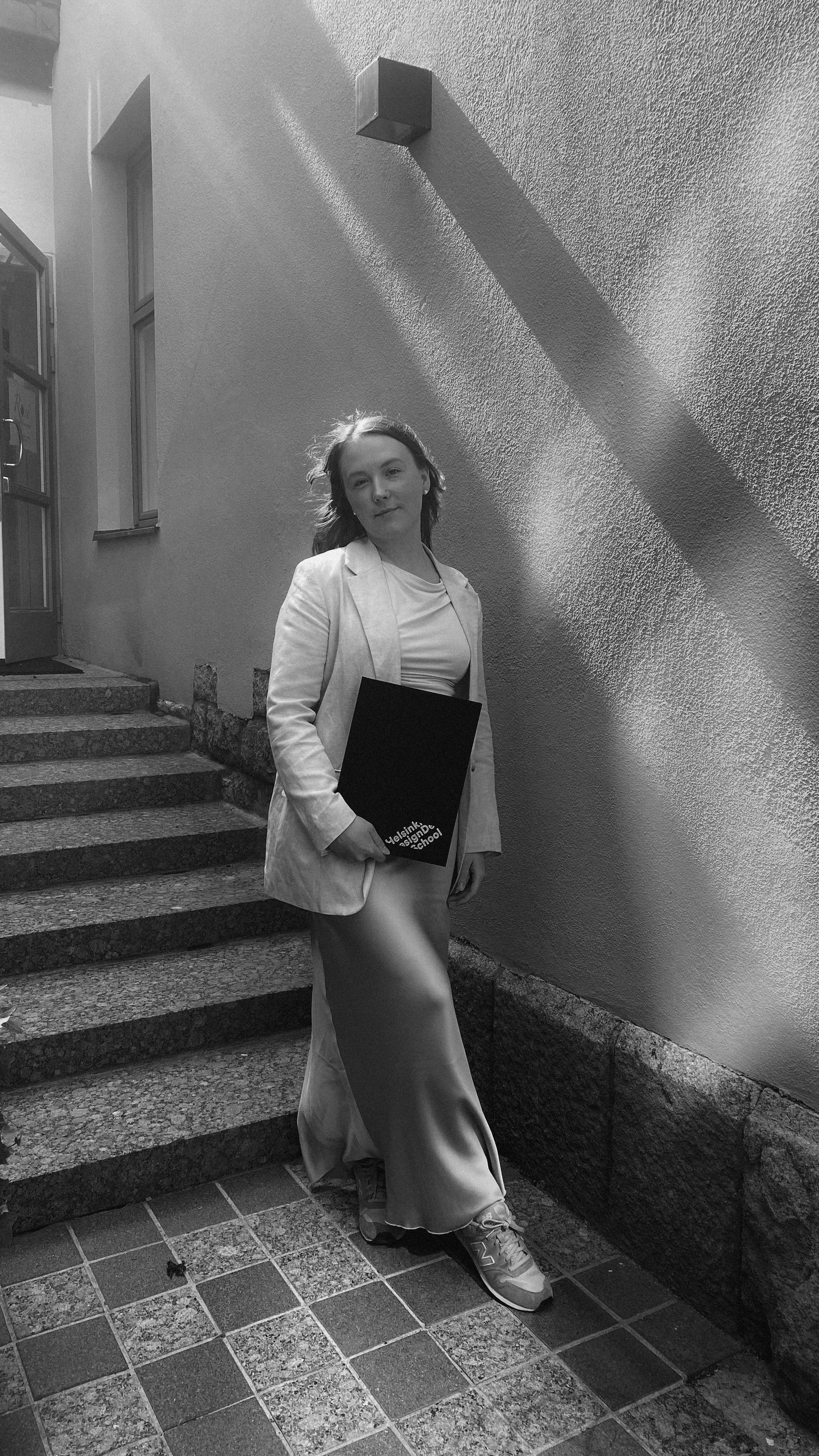 Black and white image of a person standing on tiled steps next to a white wall with dramatic shadows.