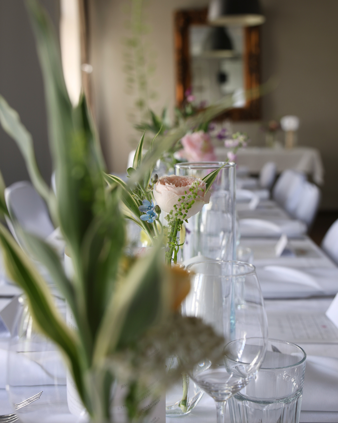 Elegant dining table set with white linens, crystal glasses, and fresh floral centerpieces in a bright restaurant.