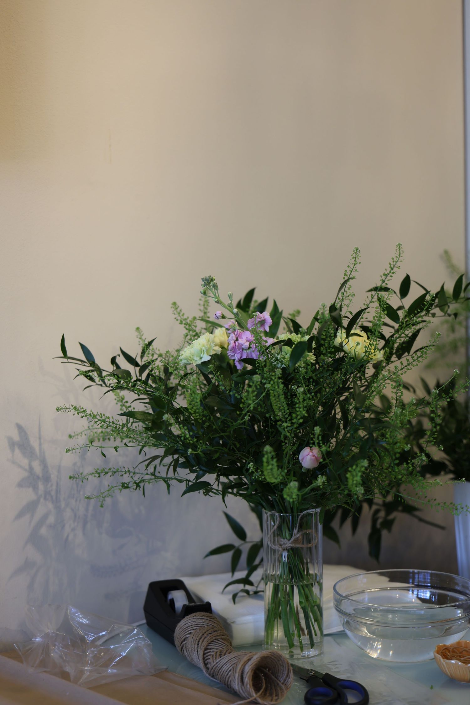 A fresh floral arrangement with purple blooms and green foliage displayed in a clear glass vase on a light surface.